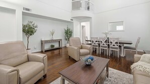 A spacious living room with a high ceiling, a dining area with a white table and chairs, and a balcony with a railing. - Oxnard Summer Escape with Pool + Hot Tub (Oxnard)