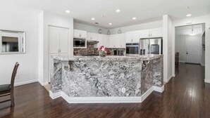 A modern kitchen with white cabinetry, a marble island, and built-in appliances. - Oxnard Summer Escape with Pool + Hot Tub (Oxnard)