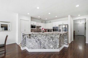 A modern kitchen with white cabinetry, a marble island, and built-in appliances. - Oxnard Summer Escape with Pool + Hot Tub (Oxnard)
