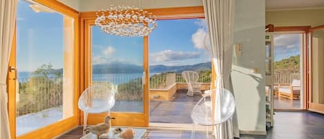 A spacious room with large windows, a glass coffee table, and a view of the mountains.