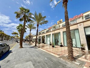 A commercial street with palm trees, a buffet restaurant, and a shopping area. - Magnificent beachfront apartment (Playa De Los Cristianos)