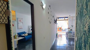 A hallway with a blue sofa, a clock on the wall, and a kitchen area in the background. - RenTenerife El Romantico (Galletas, Las)