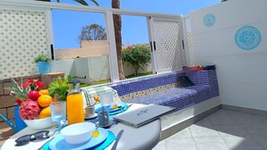An outdoor patio with a tiled seating area, a table with breakfast items, and a laptop. - RenTenerife El Romantico (Galletas, Las)