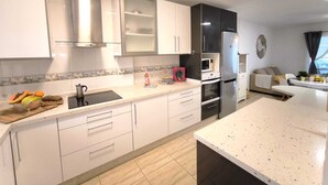 Une cuisine moderne avec des meubles blancs, un réfrigérateur en acier inoxydable, un four à micro-ondes et un coin repas comprenant un canapé et une table.