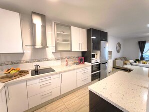 Eine moderne Küche mit weißen Schränken, einem Edelstahl-Kühlschrank, einer Mikrowelle und einem Essbereich mit einer Couch und Tisch.