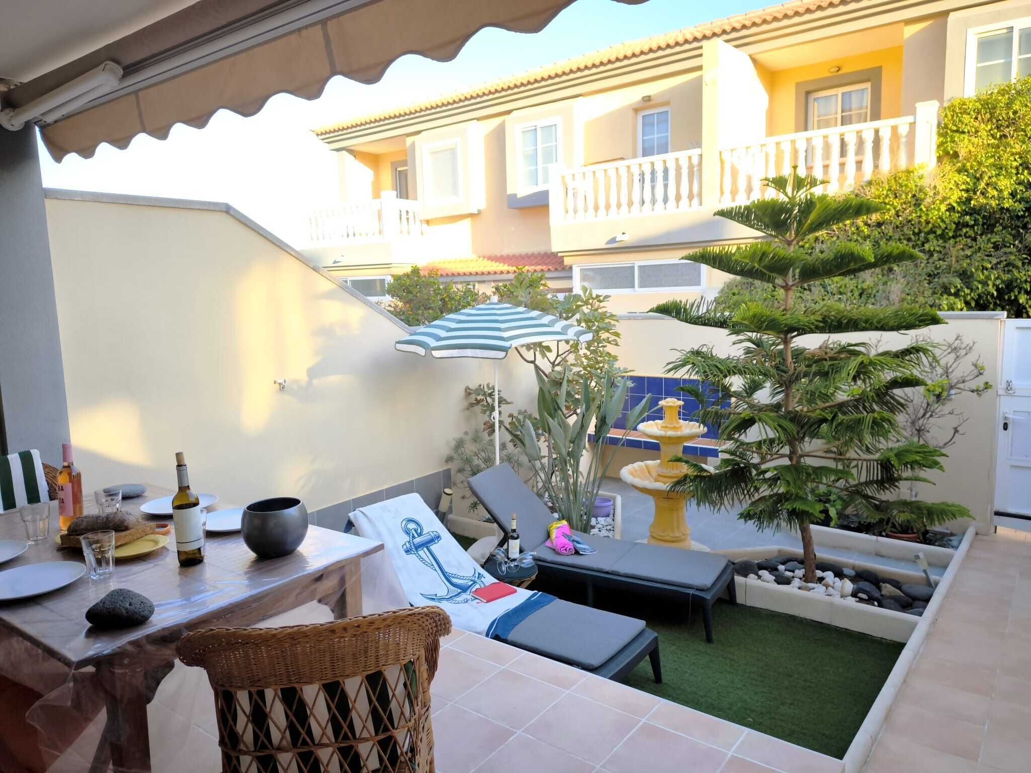 Eine Terrasse mit Esstisch, Lounge-Stühlen, einem kleinen Brunnen und einem Topfbaum.