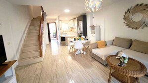 Un salon moderne avec un escalier, un coin repas et une cuisine en arrière-plan.