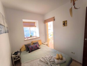 Un dormitorio con cama, mesita de noche, ventana con persianas y vistas al exterior.