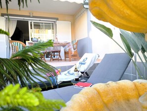 Un área exterior con sol, sillas de descanso, una mesa y vistas al interior del edificio.