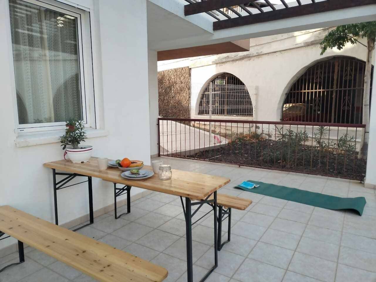 Un patio con una mesa de madera, bancos y un tapete verde.