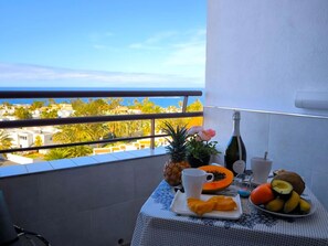 A balcony with a table set for breakfast, including fruits, a bottle, and a cup. - RenTenerife Adeje Sea Views Horizon (Costa Adeje)