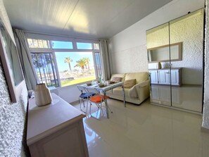 Una sala de estar moderna con comedor, un sofá, una mesa y un ventanal con vistas a palmeras.