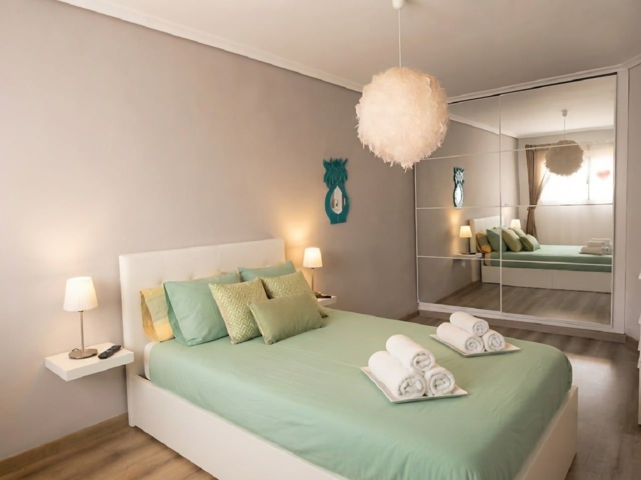 Une chambre à coucher moderne avec un grand lit, des lampes de chevet, un miroir et un objet décoratif fixé au mur.