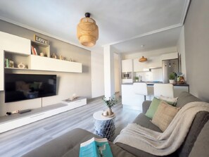 A modern living room with a flat-screen TV, a sofa, a coffee table, and a kitchen in the background. - Rentenerife Casa Lola Medano Beach (Medano, El)