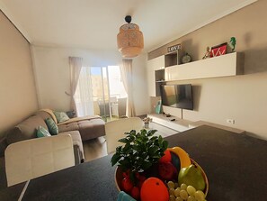A modern living room with a sofa, a dining area with a fruit bowl, a TV, and a 'LOVE' sign on the wall. - Rentenerife Casa Lola Medano Beach (Medano, El)