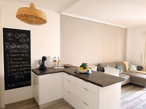 A modern kitchen with a chalkboard listing house rules, a coffee maker, and a fruit bowl on the counter. - Rentenerife Casa Lola Medano Beach (Medano, El)