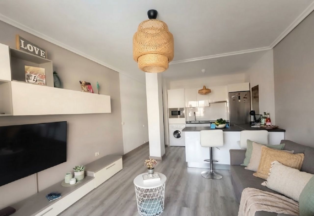 Un salon moderne avec un téléviseur à écran plat, une table basse ronde et un canapé. Il y a également un coin cuisine avec une table à manger et des tabourets de bar.