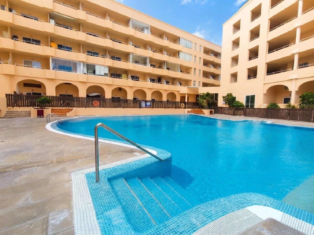 Une piscine dont le bord est recouvert de carreaux, entourée d’un immeuble à plusieurs étages doté de balcons.