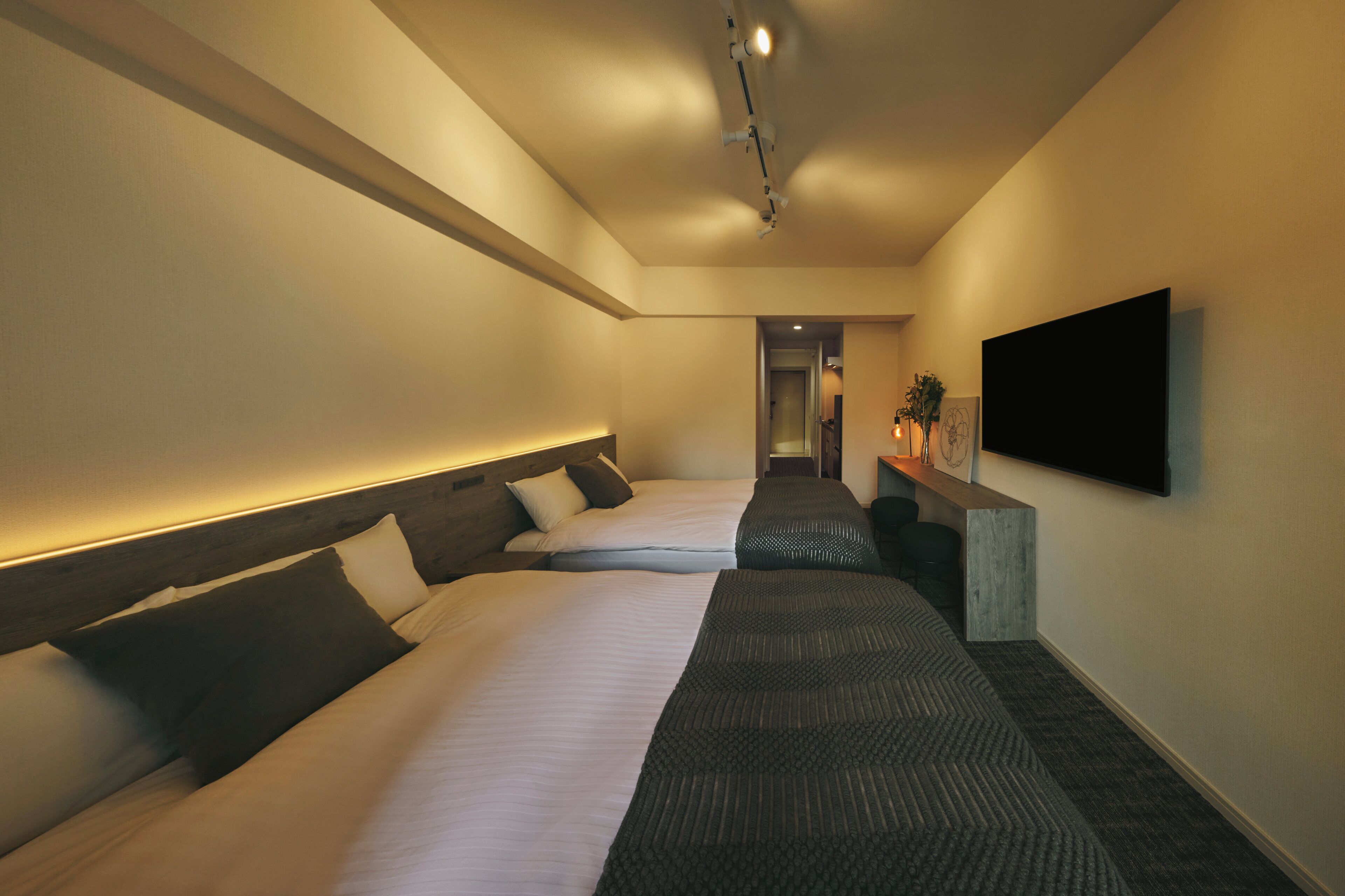A hotel room with two beds, a flat-screen TV mounted on the wall, and a small desk with a plant.