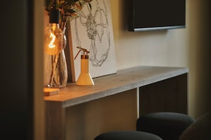 Una estantería de madera con un florero de vidrio, un candelabro metálico y una obra de arte colgada en la pared.