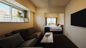 A compact hotel room with a sofa, a small table with a glass, and a bed with a view of the cityscape. - Residence Hotel Hakata Sumiyoshi (Fukuoka)
