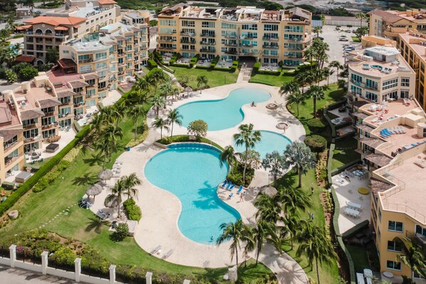 A resort with multiple swimming pools, palm trees, and a well-maintained lawn. - Eagle Beach - 3bed - 3 Bath - Ocean View - Oceania (Oranjestad)