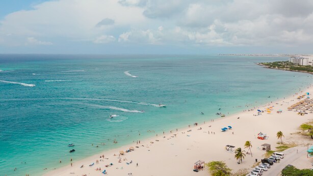 A beach with clear turquoise waters, a sandy shore, and a row of parked cars. - Eagle Beach - 3bed - 3 Bath - Ocean View - Oceania (Oranjestad)