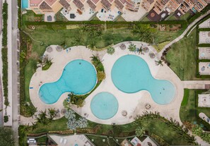 An aerial view of a resort with two large swimming pools, surrounded by palm trees and lounge chairs. - Eagle Beach - 3bed - 3 Bath - Ocean View - Oceania (Oranjestad)