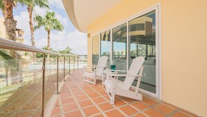 A balcony with two white chairs, a glass door, and a view of palm trees and buildings. - Eagle Beach - 3bed - 3 Bath - Ocean View - Oceania (Oranjestad)