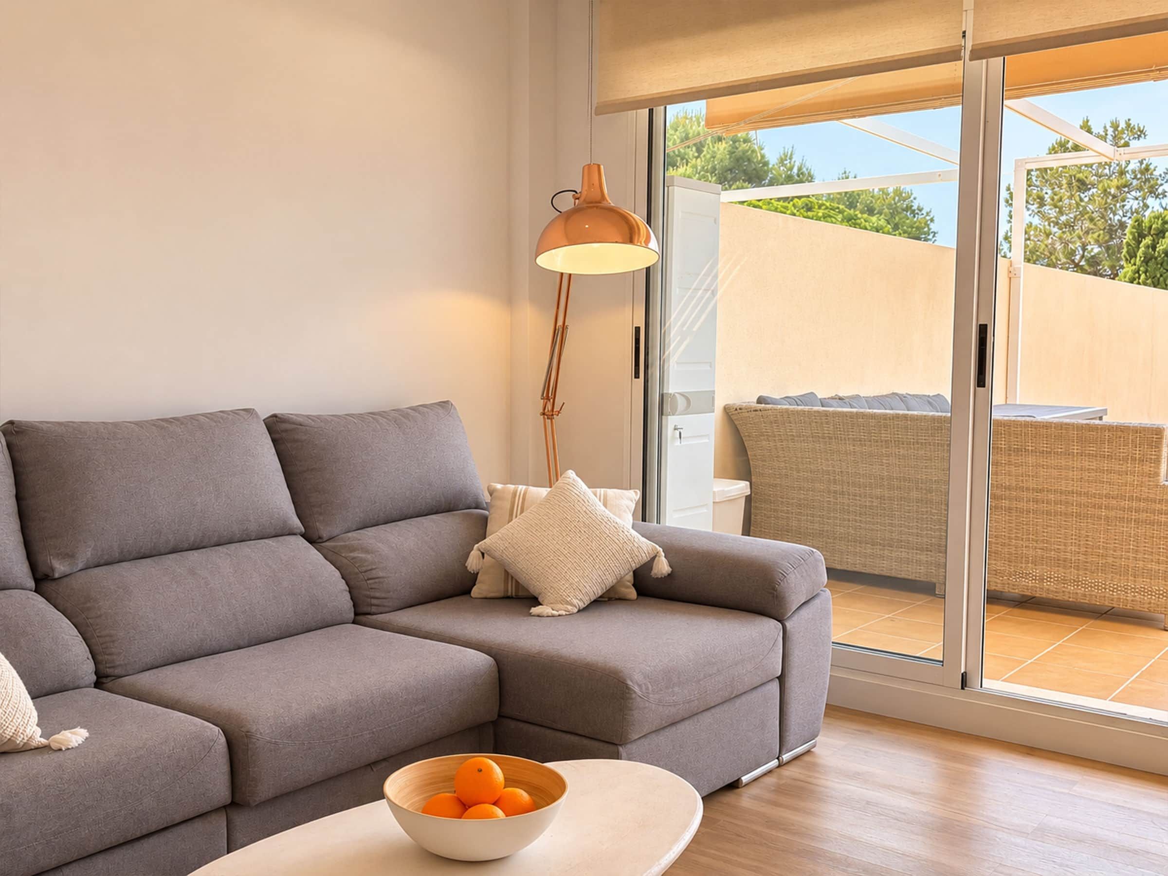 A modern living room with a grey sofa, a white bowl with oranges, and a floor lamp.