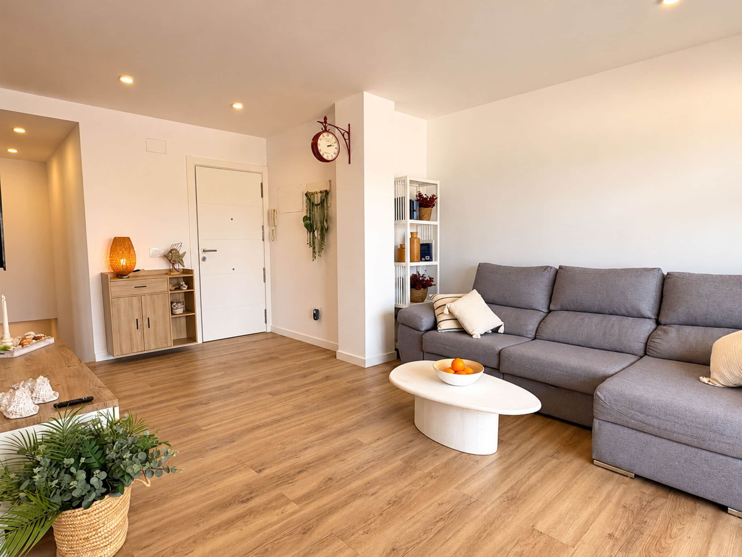 Ein modernes Wohnzimmer mit einem grauen Sofa, einem weißen Couchtisch und einem Holzboden.