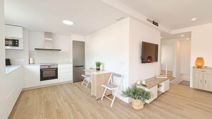 A modern kitchen with white cabinets, a built-in oven, and a dining area with a wooden table and chairs. - 06 Viridis - Golf Terrace - Oliva Nova (Oliva)