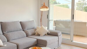 A modern living room with a grey sectional sofa, a white coffee table with a bowl of oranges, and a floor lamp. - 06 Viridis - Golf Terrace - Oliva Nova (Oliva)