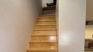 Een houten trap die uitkomt op een vloer met een keuken in de achtergrond.