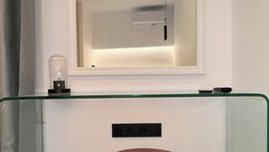 Een kamer met een glazen tafel, een ronde poef, een wandgemonteerde televisie en een raam met gordijn.