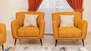 Two mustard-colored armchairs with white textured cushions, positioned in a room with a tiled floor and a white wall.