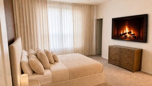 Une chambre à coucher comprenant un lit, une table de chevet, une commode, un téléviseur et une cheminée.