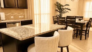 Une cuisine avec des meubles de couleur sombre, un plan de travail en granit et un coin repas comprenant une table et des chaises.