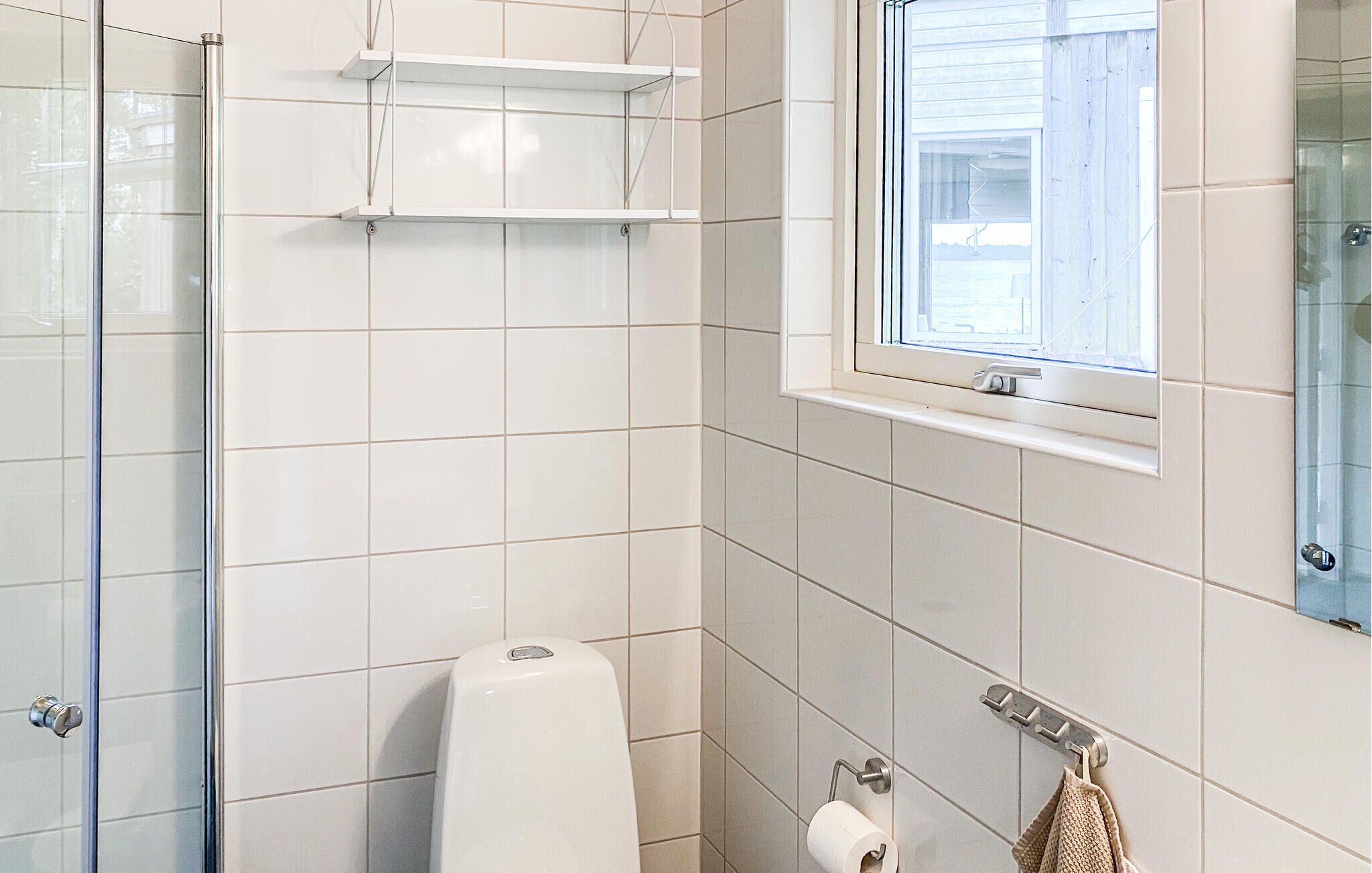 Une salle de bain carrelée de blanc, avec une douche en verre, des toilettes, un porte-serviettes et une fenêtre donnant sur un beau paysage.