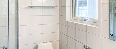 Une salle de bain carrelée de blanc, avec une douche en verre, des toilettes, un porte-serviettes et une fenêtre donnant sur un beau paysage.
