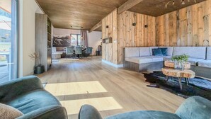 Ein großzügiger Wohnbereich mit Holzboden, einer Couch, einem Esstisch mit Stühlen und Blick durch ein großes Fenster.