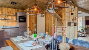 Ein Holzinterieur mit einem Esstisch für sechs Personen, einer Küchenzeile und einer Treppe.