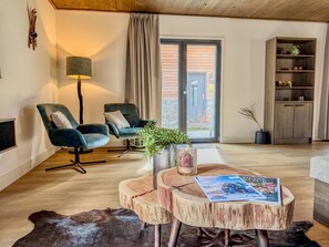 Ein modernes Wohnzimmer mit zwei dunkelblauen Sesseln, einem Holztisch mit einer Zeitschrift, einer Stehlampe und Blick durch eine Glastür.