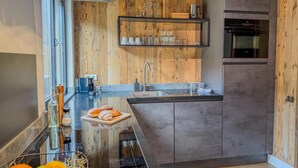 Eine moderne Küche mit Holzvertäfelung, einem eingebauten Ofen und einer Kochinsel mit Glasplatte, belegt mit Früchten und Gebäck.
