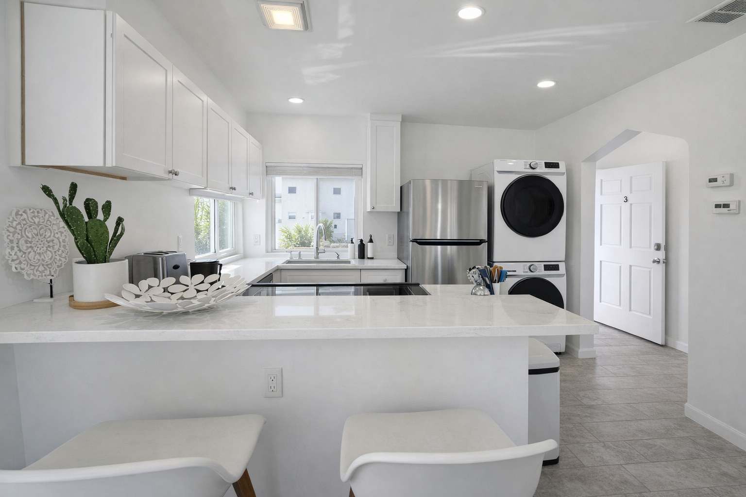 Una cocina moderna con armarios blancos, una isla central, un refrigerador de acero inoxidable y lavadora y secadora integradas.
