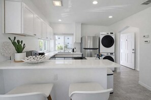 A modern kitchen with white cabinetry, a central island, a stainless steel refrigerator, and a built-in washer and dryer. - Newly Redone Bayview Apt Steps to Bay & Boardwalk (San Diego)