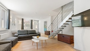 Uma sala de estar moderna com sofá, mesa de centro e escada, com uma televisão.