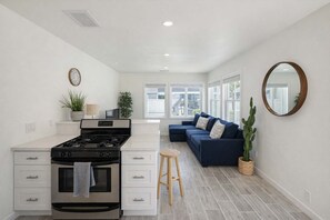 Una cocina moderna con estufa, muebles blancos y una zona de comedor con sofá azul y una planta de cactus.