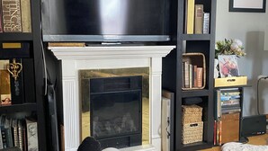 Ein Wohnzimmer mit Kamin, Fernseher und Bücherregalen.