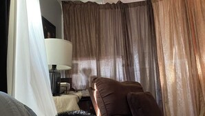 Ein Hotelzimmer mit Bett, Stuhl, Lampe und Vorhängen.